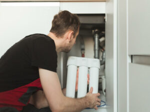 Plumber in the kitchen holding household three stage flask water purification system